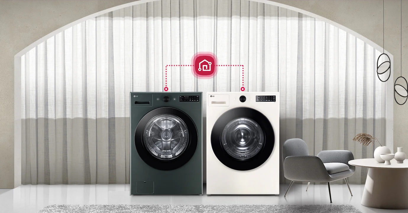 두 대의 LG 세탁기가 나란히 놓여 있으며, 각각의 세탁기 위에는 제어 패널이 있습니다. 세탁기 위에는 스마트 홈 연결을 나타내는 아이콘이 있으며, 점선으로 두 세탁기와 연결되어 있습니다. 배경에는 커튼이 드리워져 있고, 세탁기 옆에는 의자와 테이블이 놓여 있습니다. 테이블 위에는 장식용 꽃병이 있습니다.