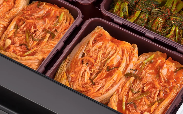 김치가 담긴 여러 개의 용기가 보입니다. 배추김치와 갓김치가 각각 용기에 정리되어 있습니다. 김치는 빨간 양념이 고루 묻어 있으며, 배추김치는 길게 절여져 있고 갓김치는 짧게 잘려 있습니다. 용기는 깔끔하게 정돈되어 있는 모습입니다.