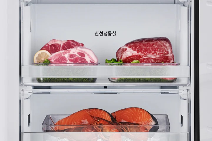 냉장고 내부에 두 개의 투명한 서랍이 보이며, 위쪽 서랍에는 신선냉동실이라는 텍스트가 있습니다. 서랍 안에는 레몬 조각과 함께 돼지고기와 소고기가 각각 놓여 있습니다. 아래쪽 서랍에는 얼음 위에 연어와 바닷가재가 담겨 있습니다.